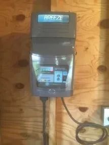 A breeze irrigation controller is hanging on a wooden wall.