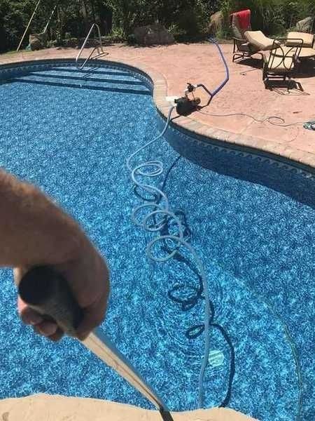 A person is holding a hose in front of a swimming pool.
