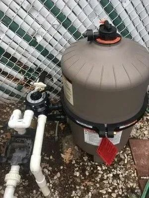A swimming pool filter is sitting on the ground next to a chain link fence.