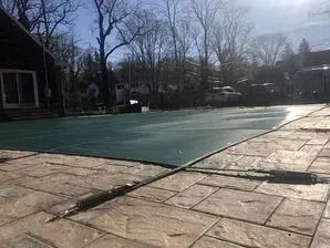 A green pool cover is sitting on top of a brick patio.