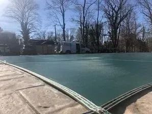 A green tarp is covering a swimming pool with trees in the background.