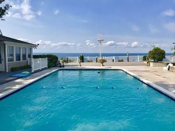 A large swimming pool with a view of the ocean and a house in the background.
