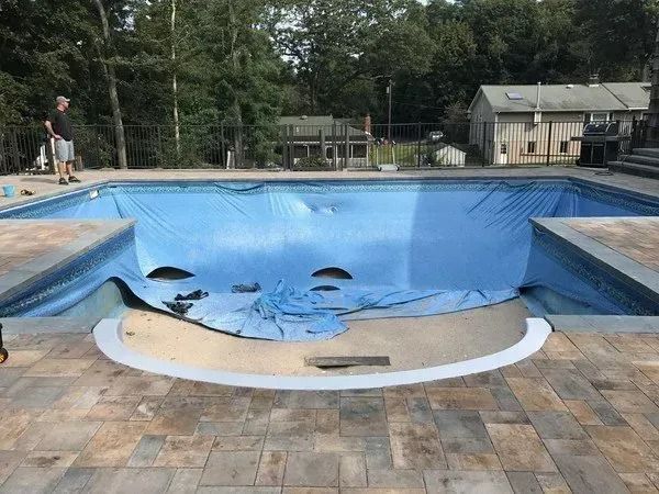A man is standing next to a large swimming pool covered in a blue tarp.