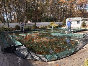 A man is standing next to a swimming pool covered in a tarp.