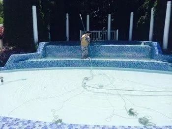 A man is cleaning a swimming pool with a broom.