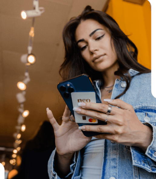 A woman in a denim jacket is holding a phone with a neo card on it