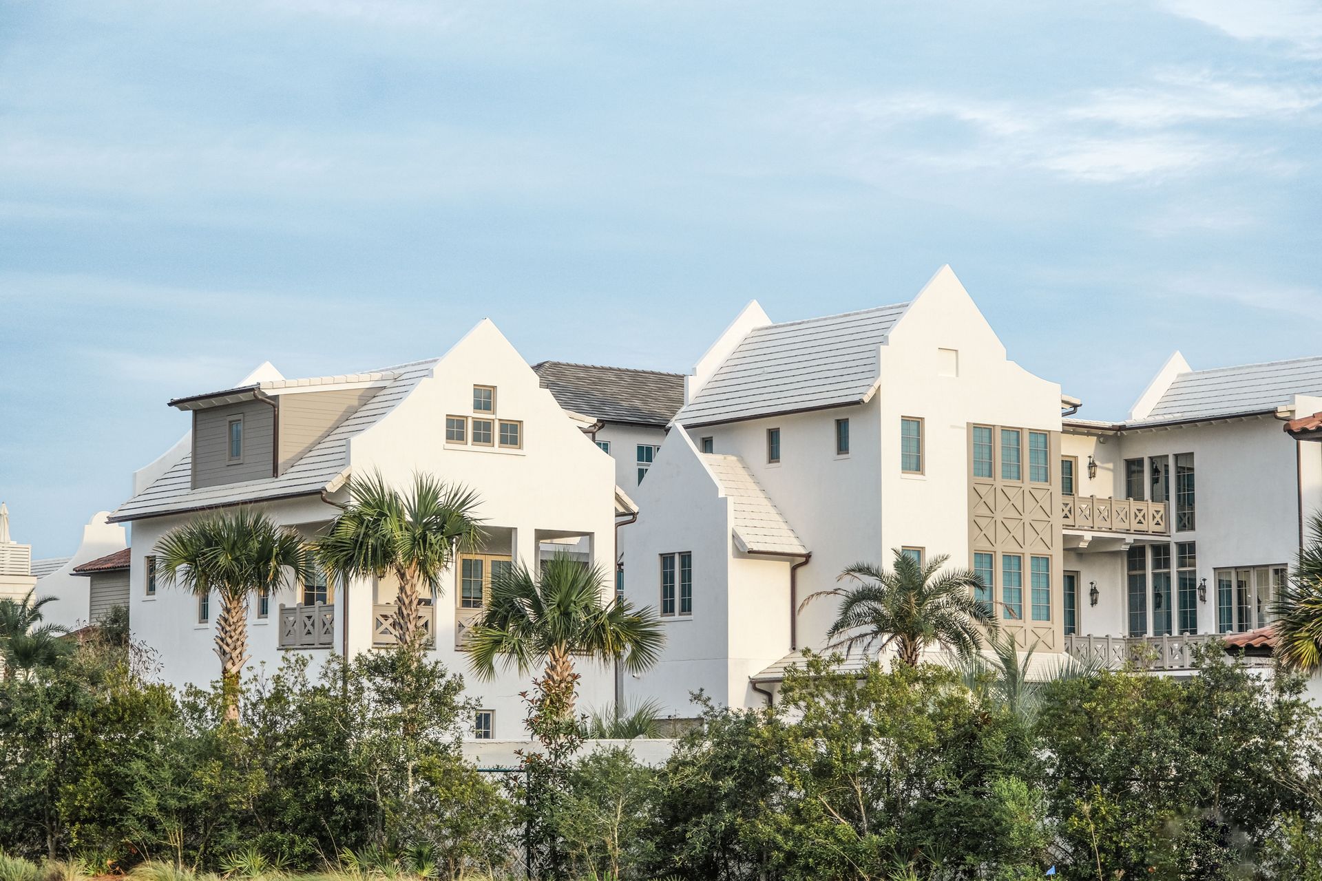 White modern houses with peaked roofs behind green trees under a blue sky