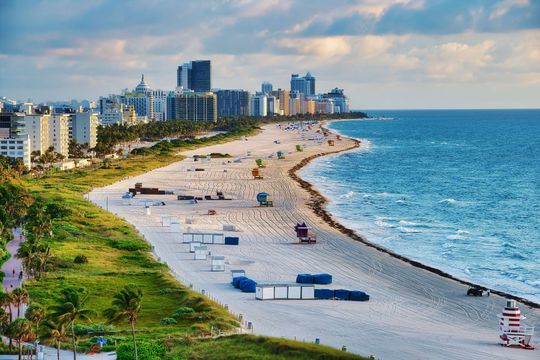 Sandy beach curving along a blue ocean beside coastal high-rises and green shoreline.