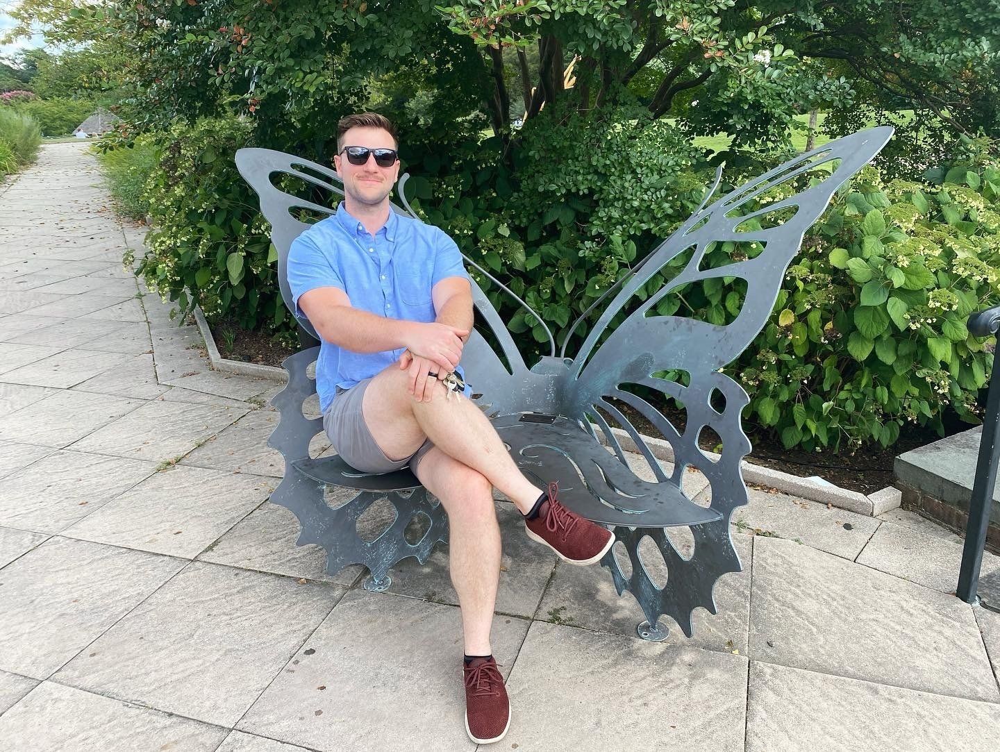 Image of RETEX's Josh Lewis on a metal butterfly bench from Lewis Ginter Botanical Gardens. Image by RETEX's Katelyn Lewis. 