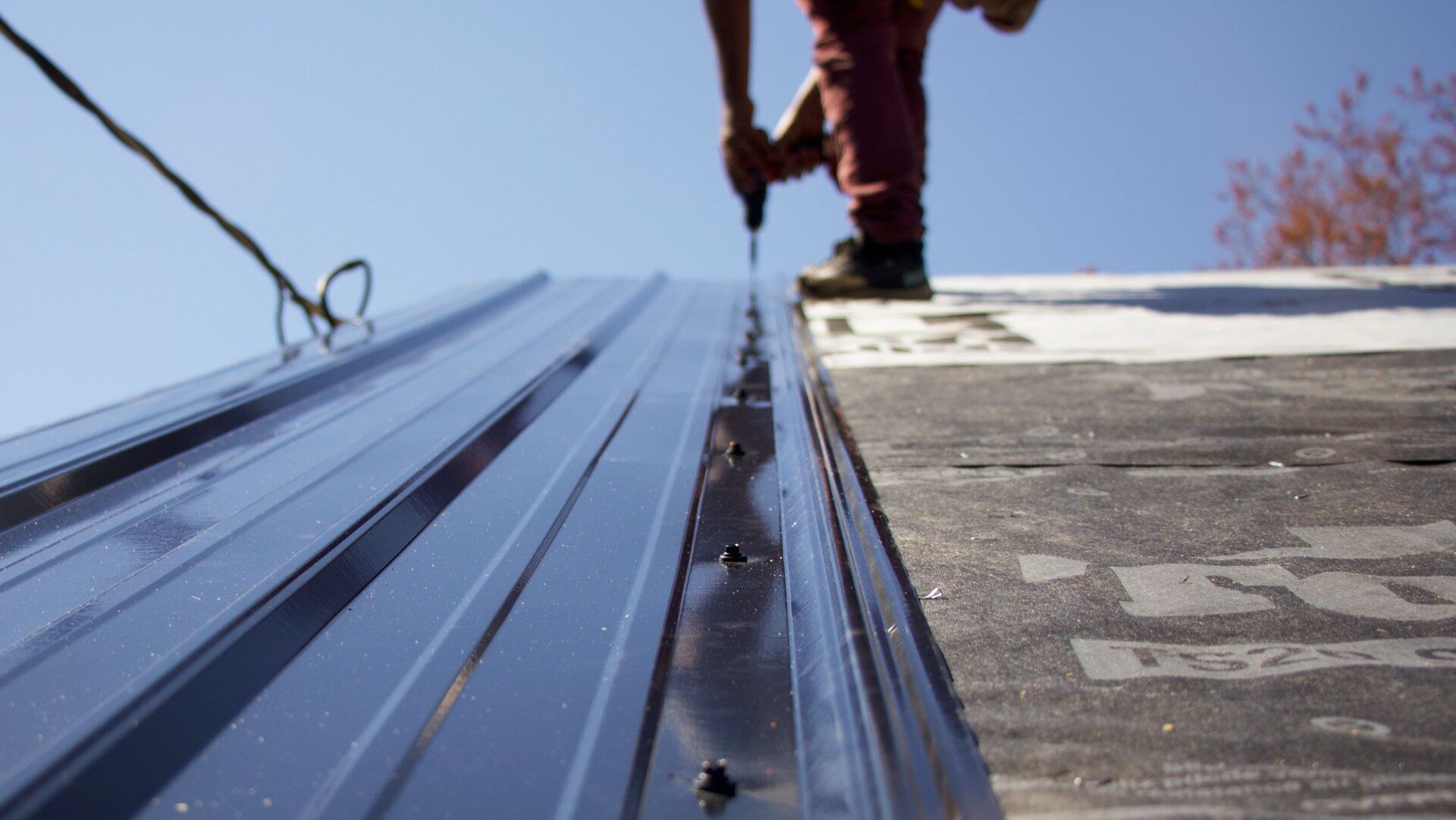 Image of RETEX crew member installing a black ribbed metal roof panel on Richmond VA home. Image by RETEX's Katelyn Lewis.