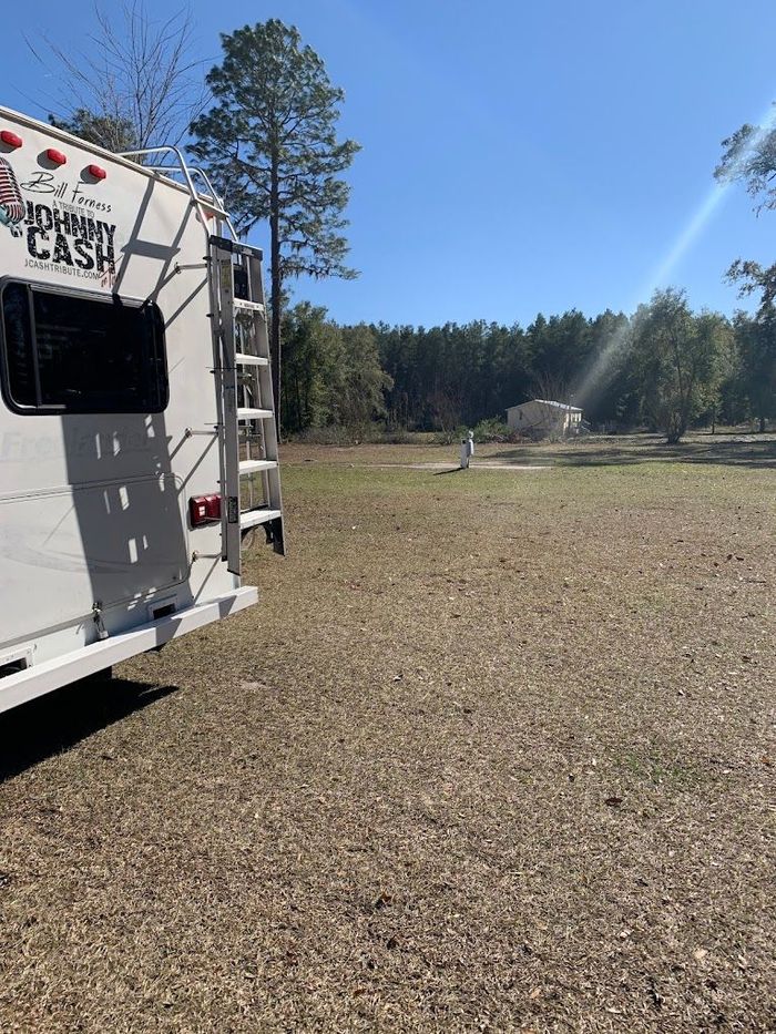 A white rv is parked in a field with trees in the background.
