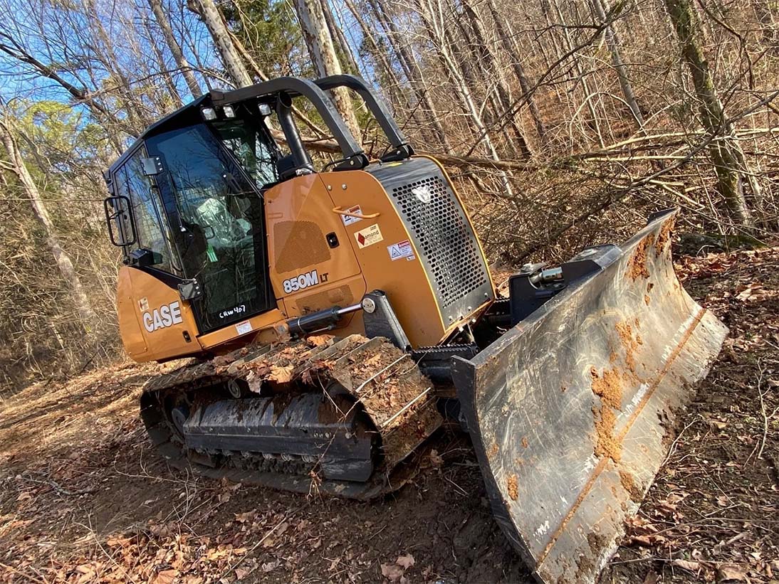 Excavator parked on field with many trees — Bethpage, TN — Michael Shaver Plumbing & Septic Pumping