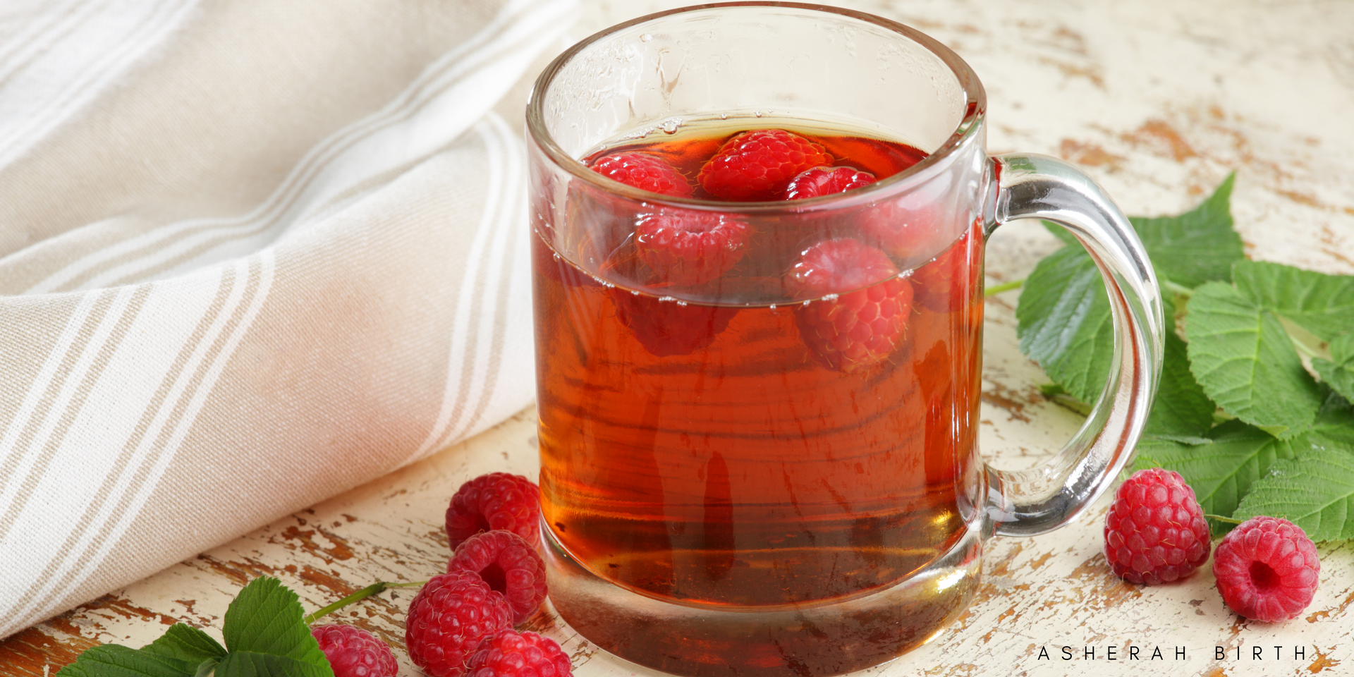 A cup of tea with raspberries and mint leaves on a table.