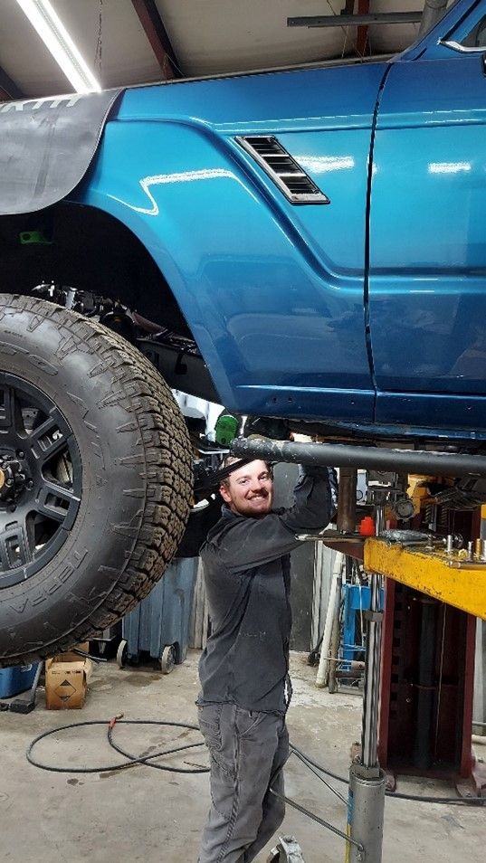 Portrait of a mechanic in black uniform examining a car in auto repair shop, professional maintenanc