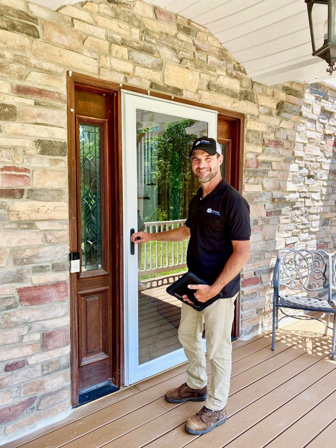 A man is standing on a porch in front of a brick building holding a tablet.