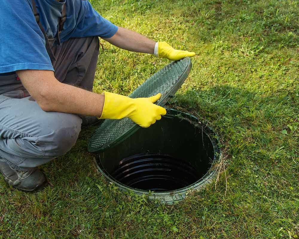 A man wearing yellow gloves is opening a manhole cover.