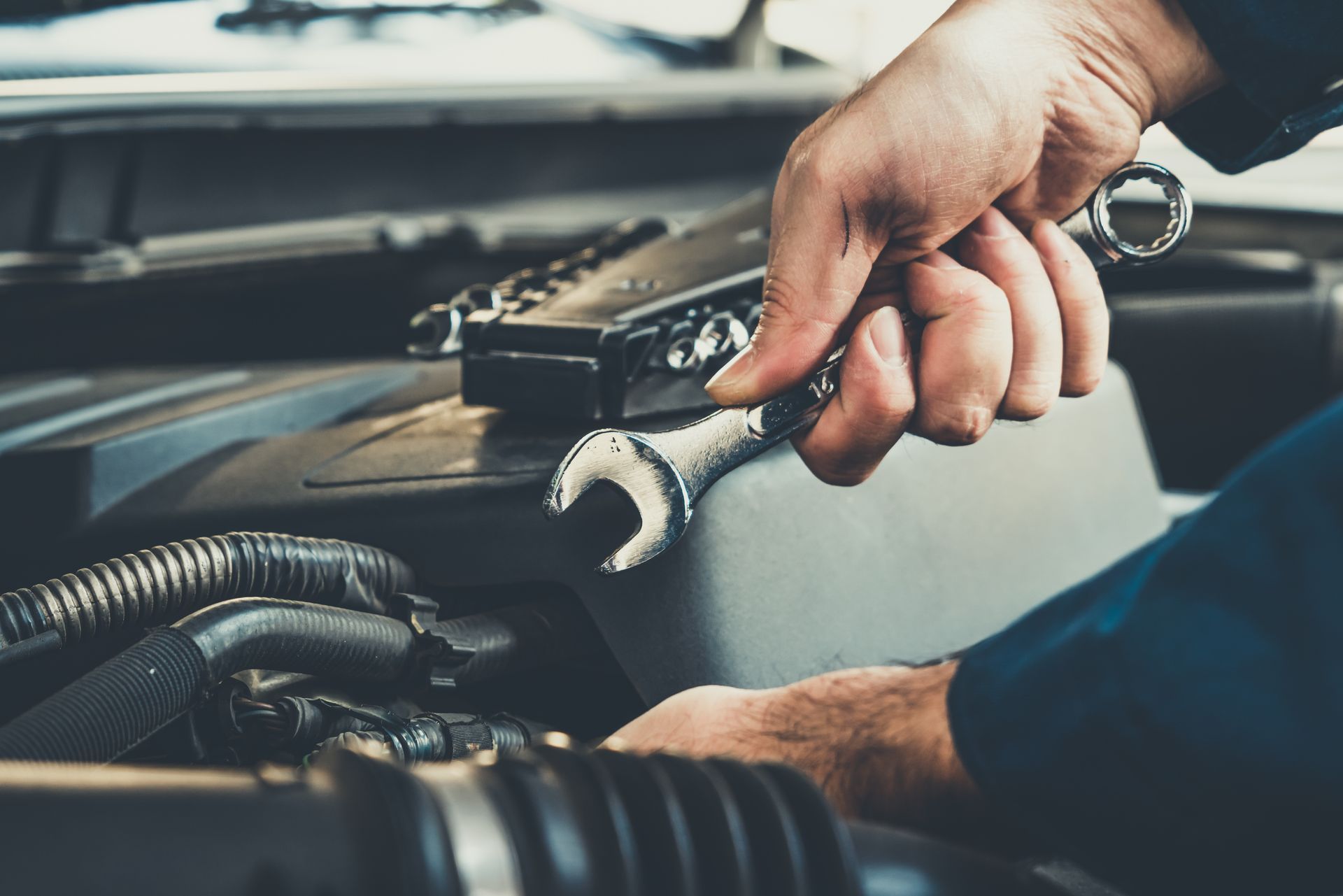 A man is working on a car engine with a wrench.