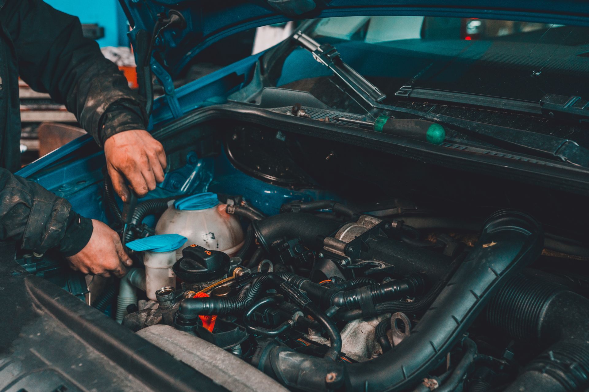A man is working on the engine of a blue car.