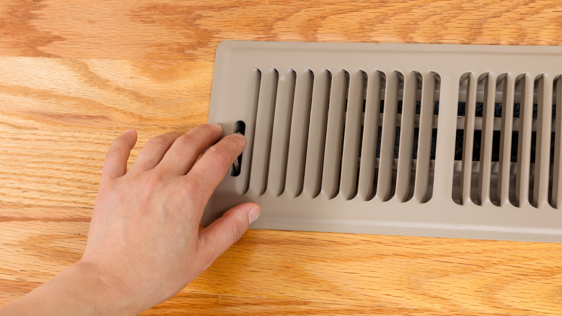 A person is closing a vent on a wooden floor.