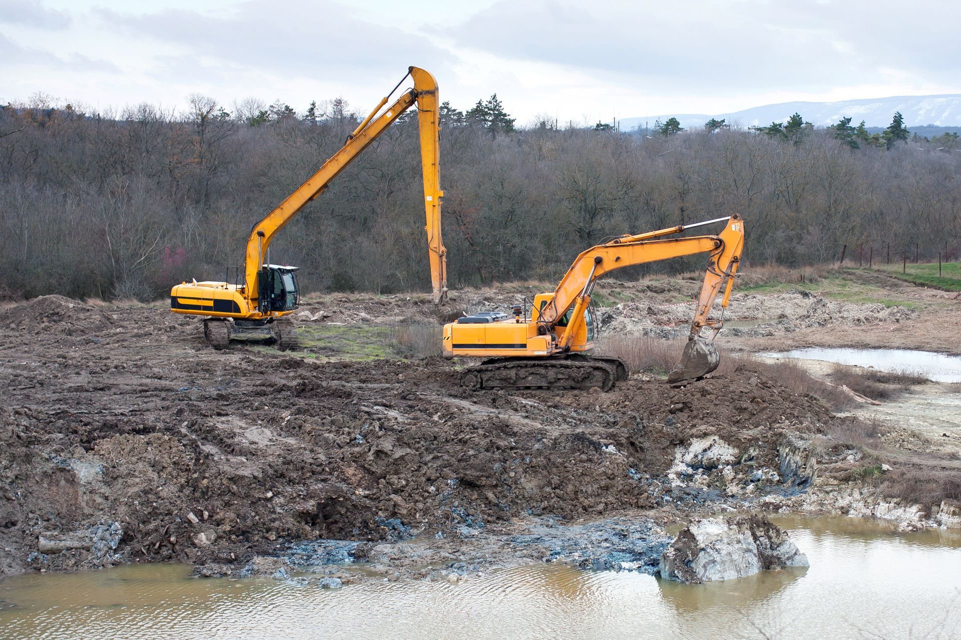 Deux excavatrices jaunes creusent dans la terre près d'un plan d'eau.