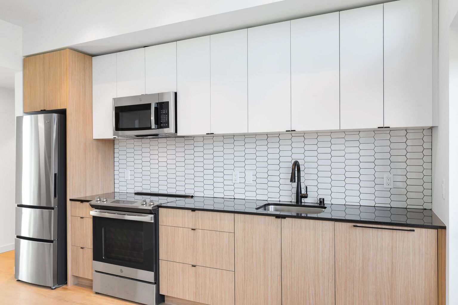 Modern kitchen with light wood and white cabinets, stainless steel appliances, and a tiled backsplash.