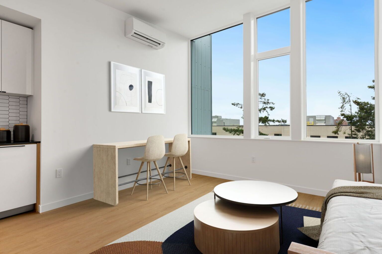 Modern apartment interior with a desk, chairs, and coffee tables near a large window.