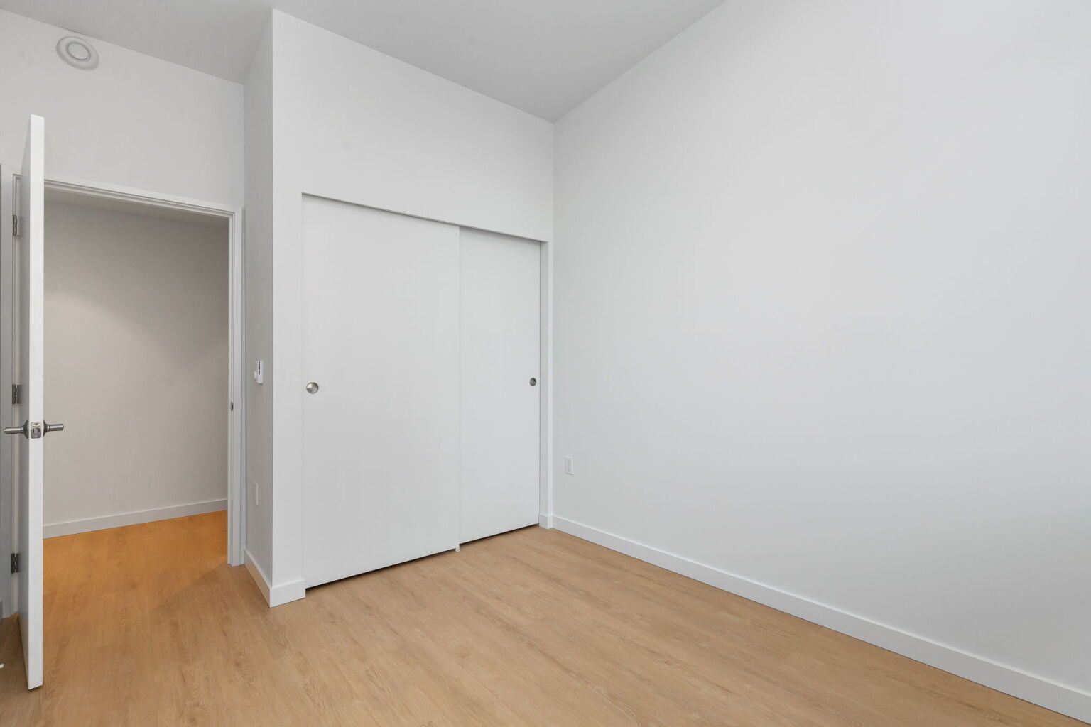 Empty room with white walls, sliding closet door, and an open doorway to a closet.