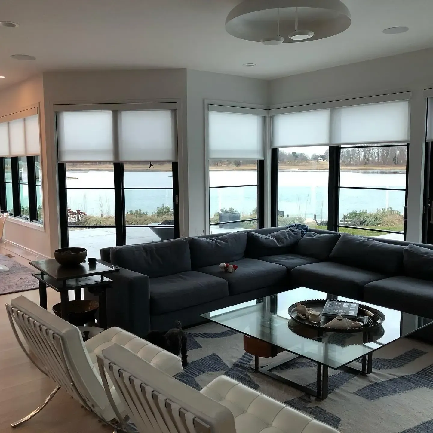 Modern living room with sectional sofa, glass coffee table, and large windows overlooking water.