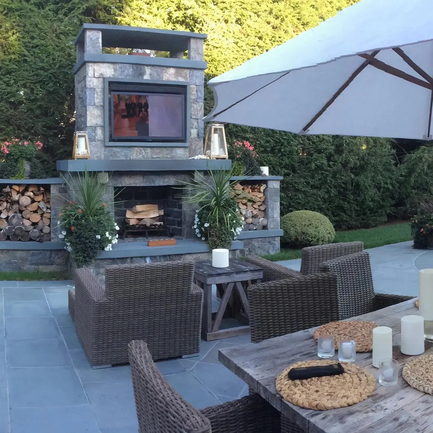 Outdoor fireplace with wood storage, seating area, and dining table on a patio.