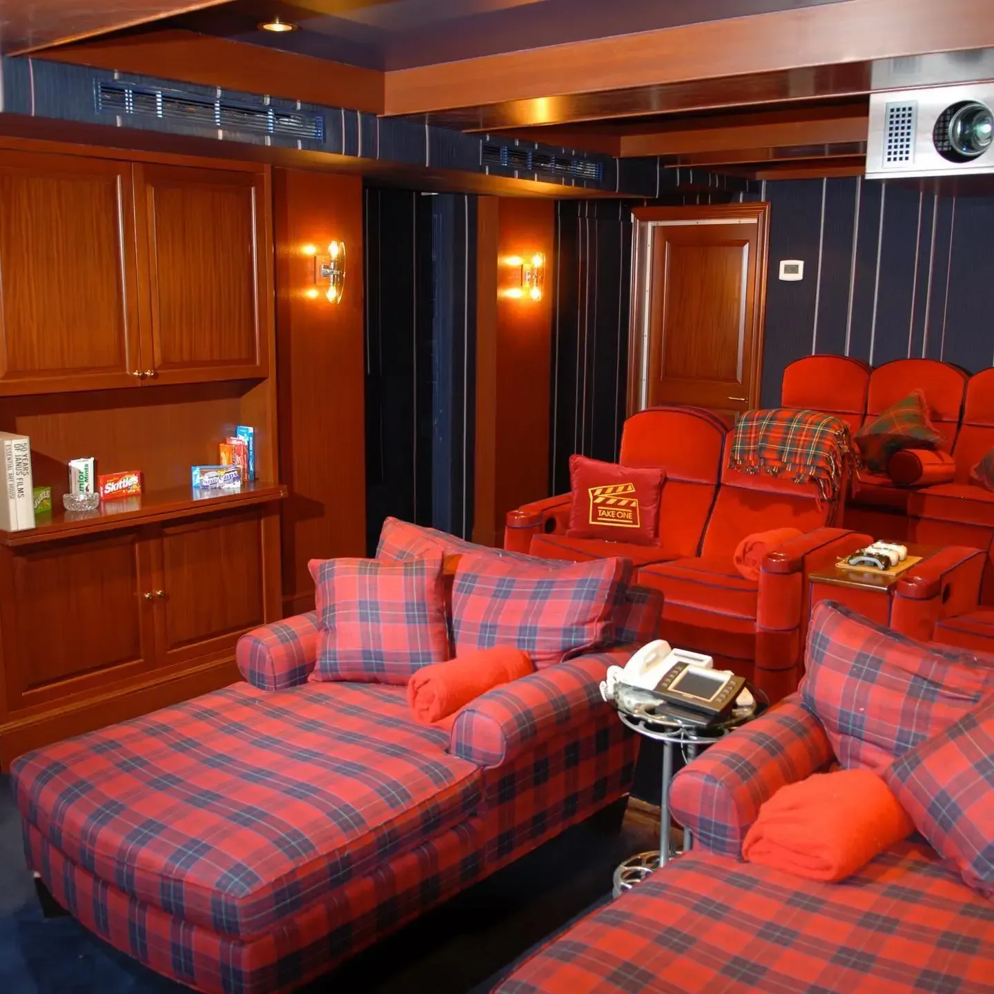 Cozy home theater with red armchairs, plaid chaise lounges, and a projector screen. Wood accents and blue walls.