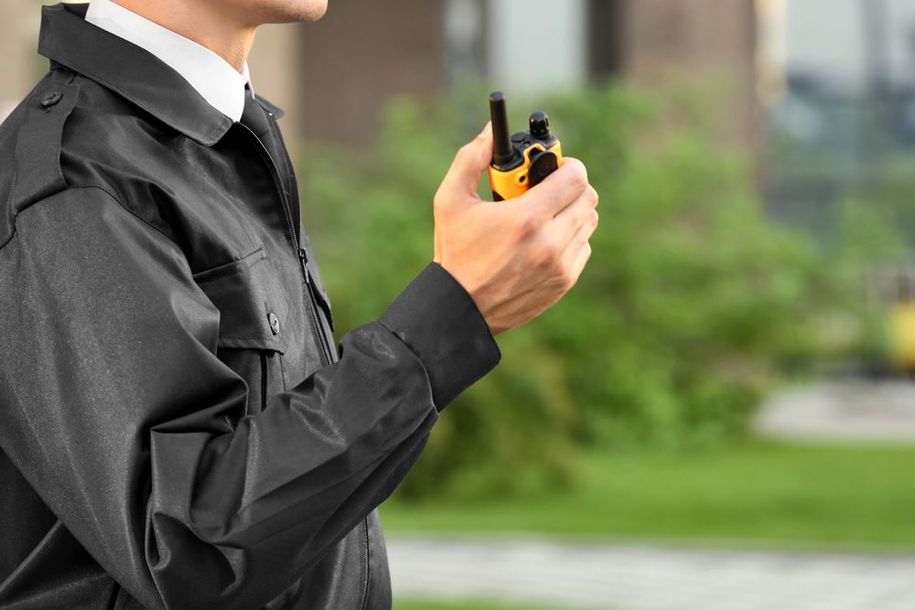 A security guard is holding a walkie talkie in his hand.