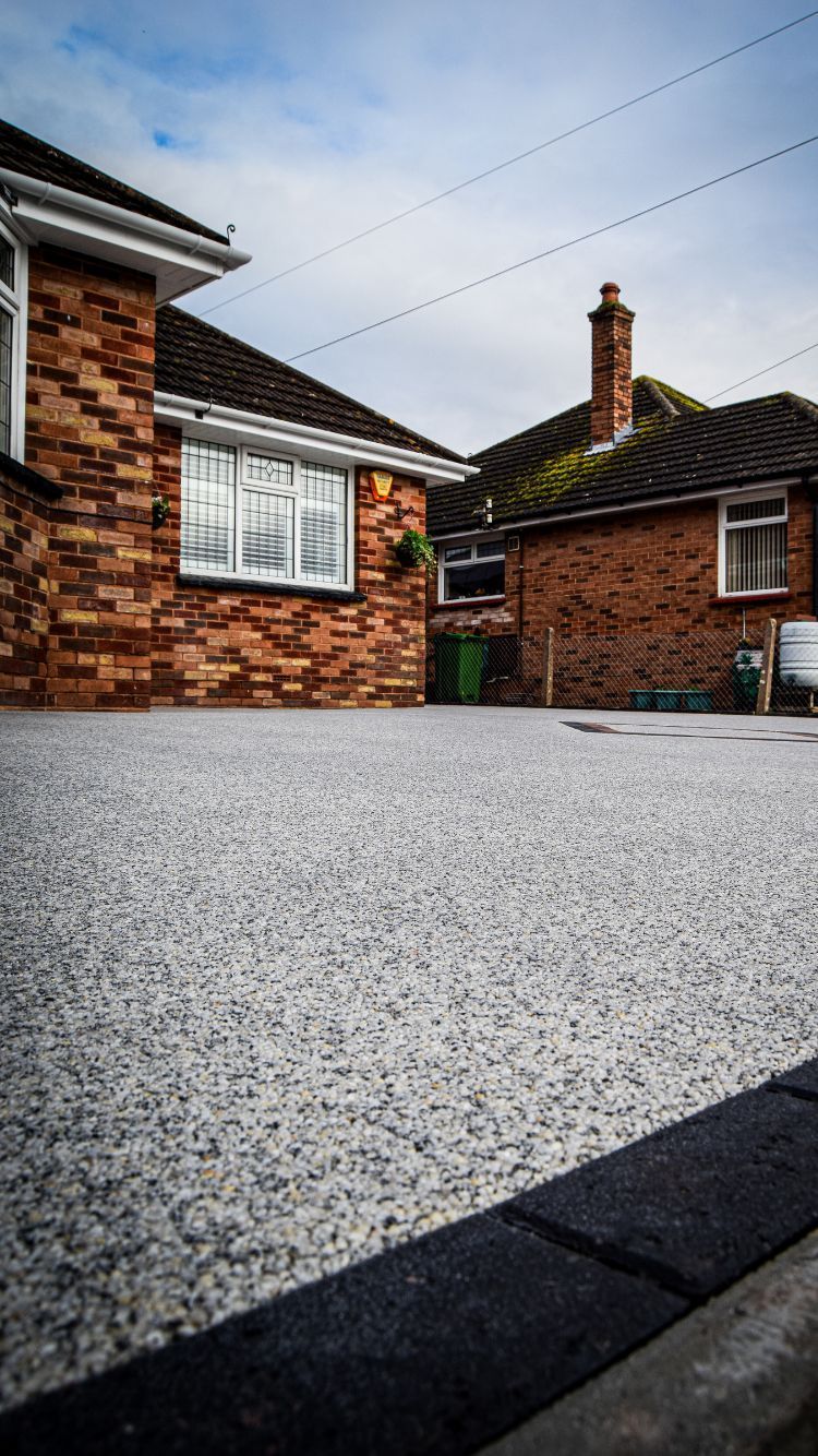 A photo of a fresh, grey resin driveway with a dark block paving border