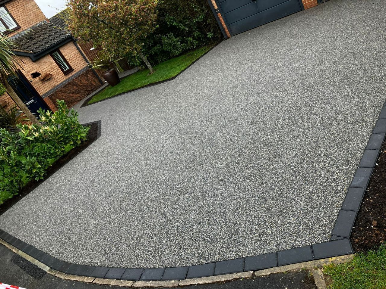 Grey resin driveway with grass patches on either side, surrounded by black block paving border