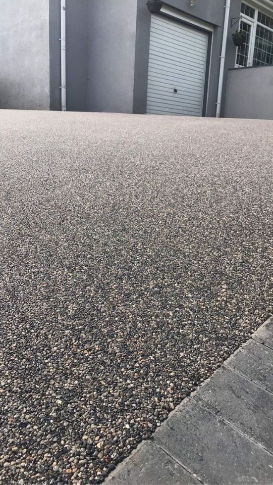 Grey resin driveway with block paving border in front of grey building and garage