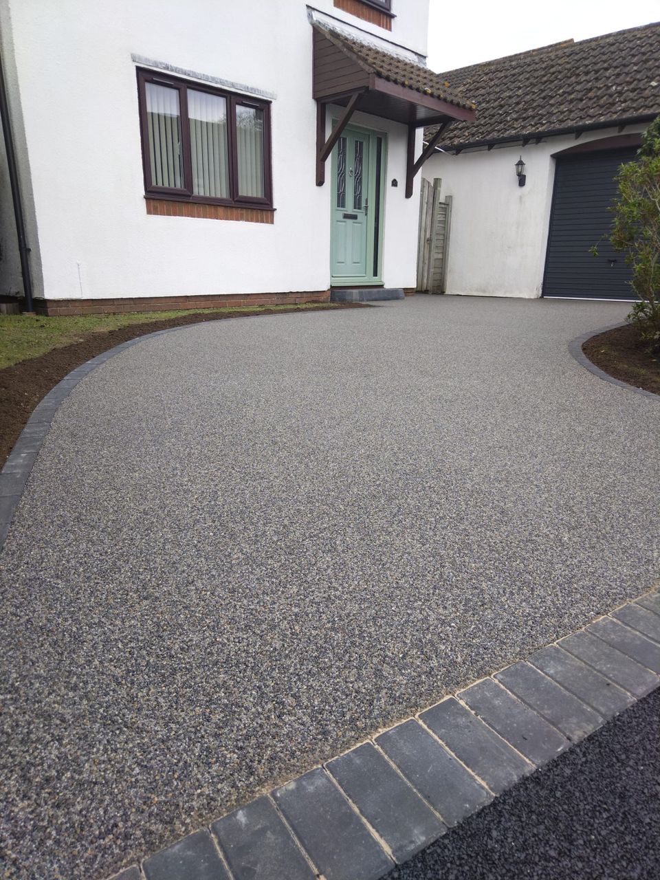 Grey resin driveway with block paving border leading up to mint green door