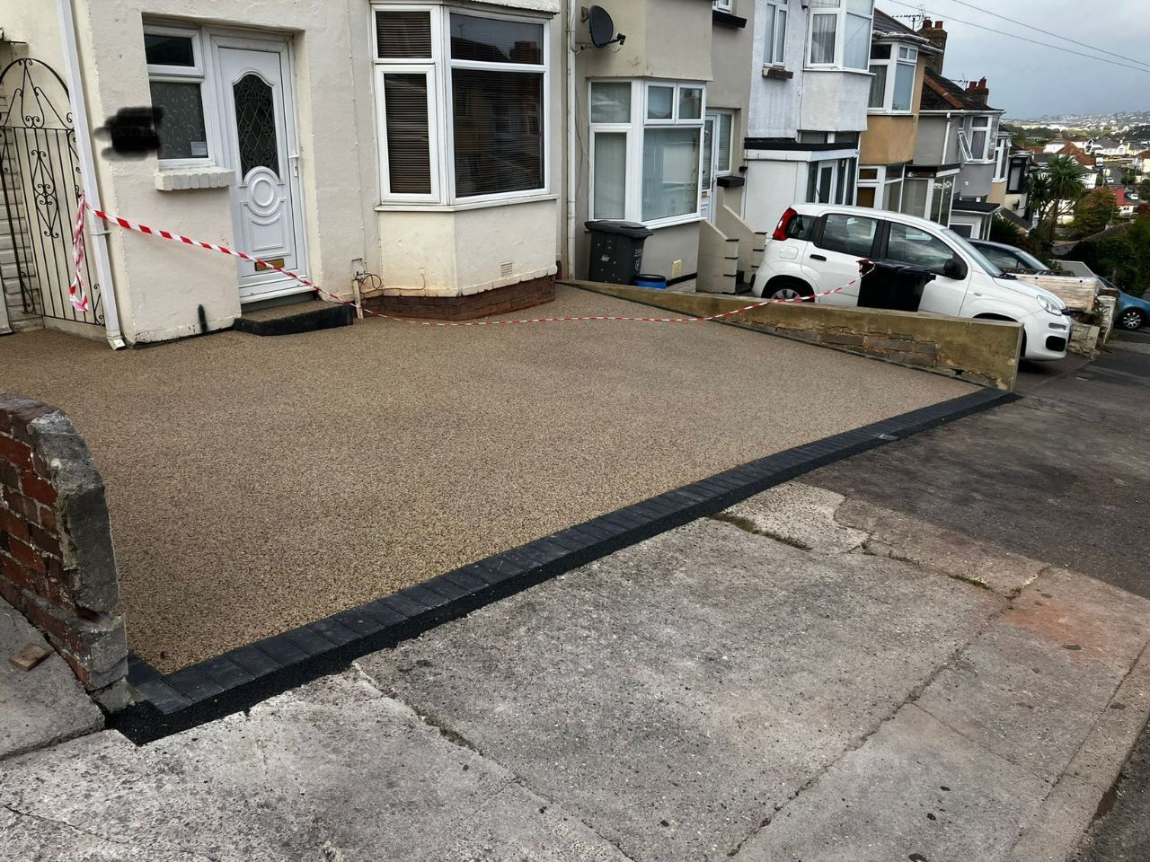 Small brown resin driveway outside cream house