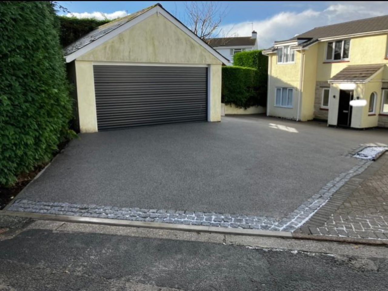 Dark grey resin driveway in front of black garage door, with black block paving border