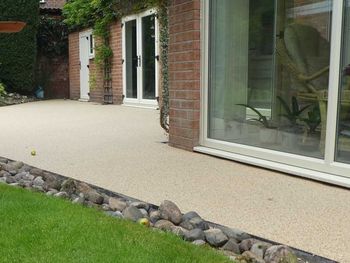 Beige resin path in front of glass windows, surrounded by stones.