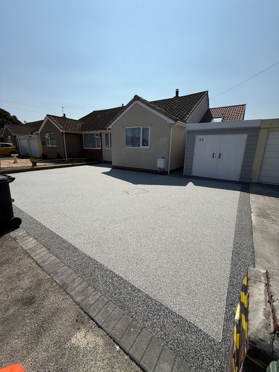 Grey resin driveway with block paving border in front of grey building and garage