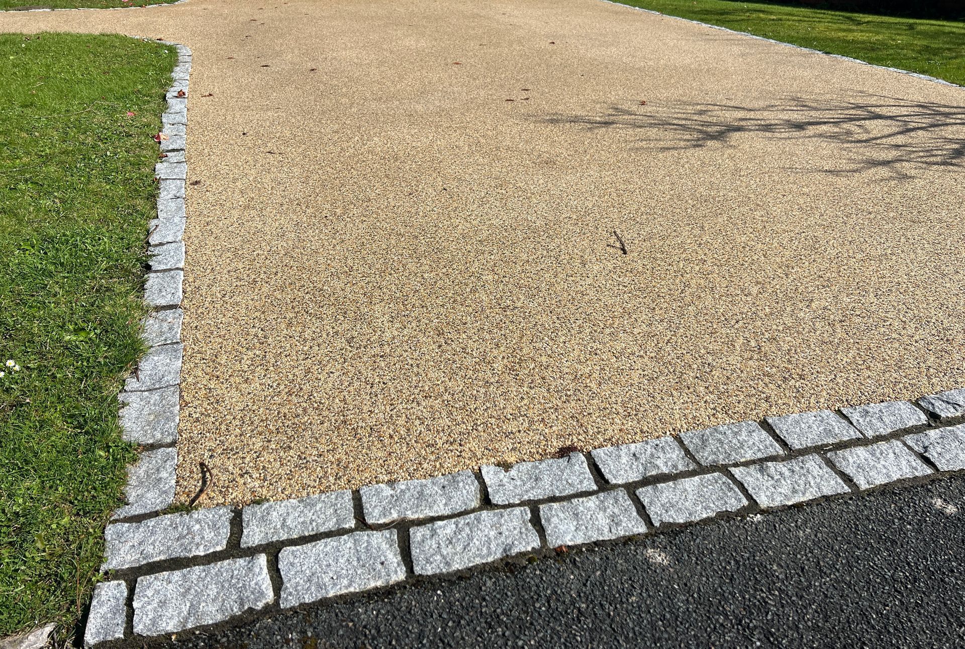 Gravel path bordered by white cobblestones beside green grass and a dark paved edge.