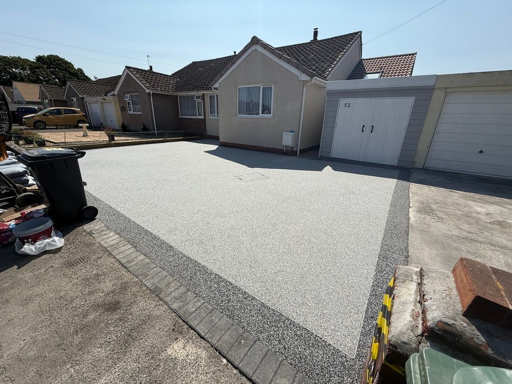 Dark grey resin driveway in front of black garage door, with black block paving border