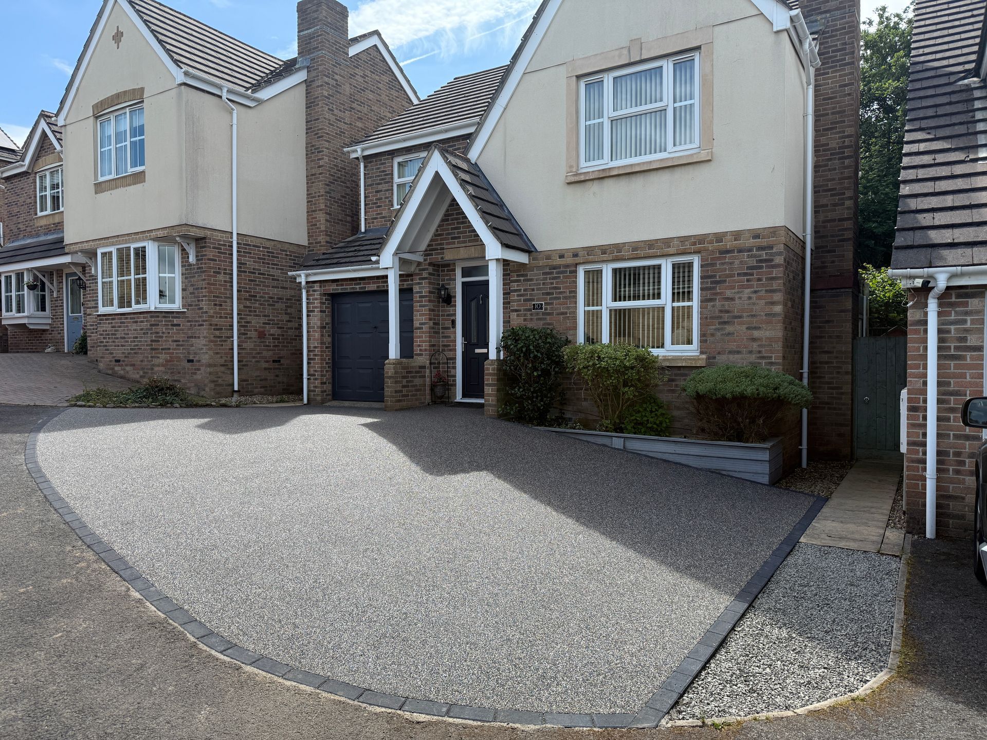 After photo of grey resin driveway in front of red brick house.