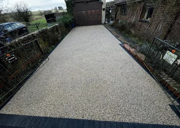 Freshly resurfaced gravel driveway leading to a garage, bordered by fences and brick walls