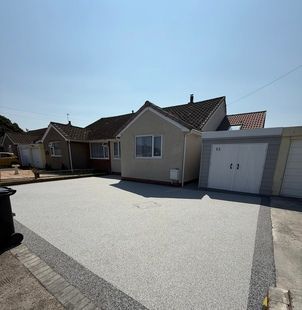 Grey resin driveway leading up to a white home and garage