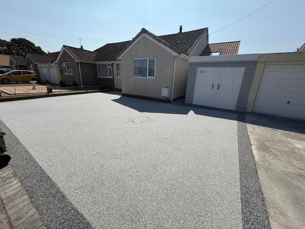 Small grey resin driveway outside of red brick house with a blue garage