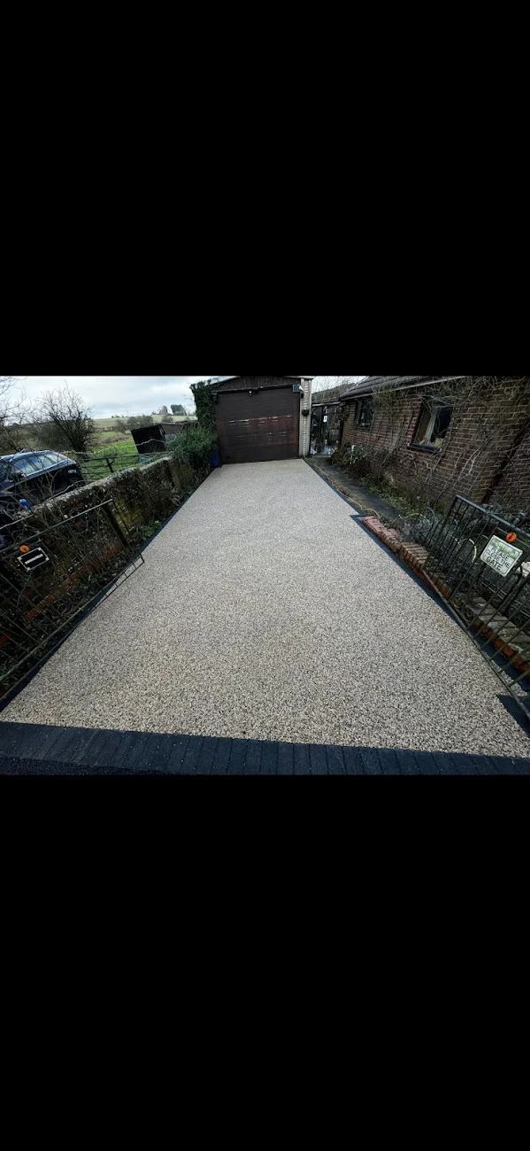A gravel driveway between brick walls leading towards a structure. The sky is overcast.