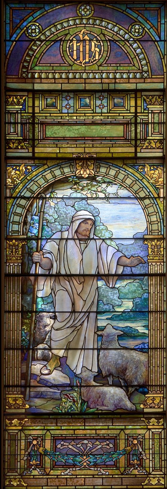 Stained glass window depicts Jesus as the Good Shepherd, holding a staff and watching over sheep in a pastoral setting.