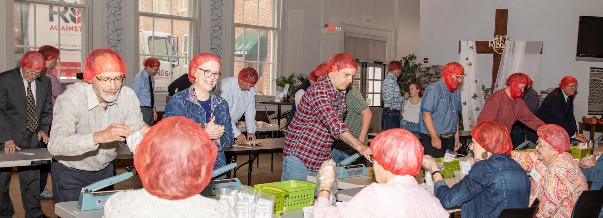 A group of people wearing red hairnets work at tables in a room.