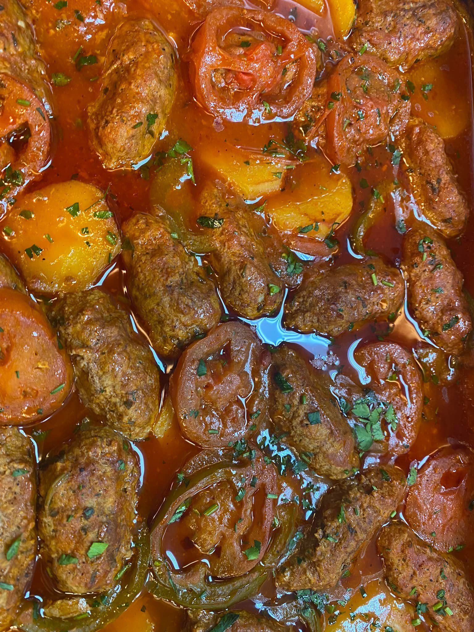 A close up of a casserole dish filled with meatballs and tomatoes.