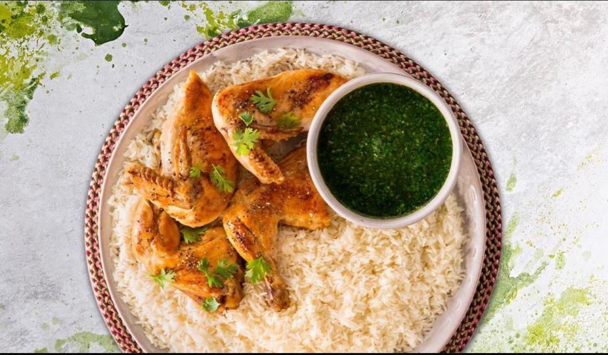A plate of food with rice and chicken and a bowl of green sauce.